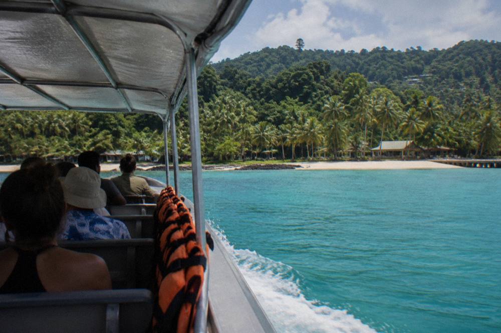 Tender boat carrying cruise passengers across turquoise water toward a palm-lined island beach