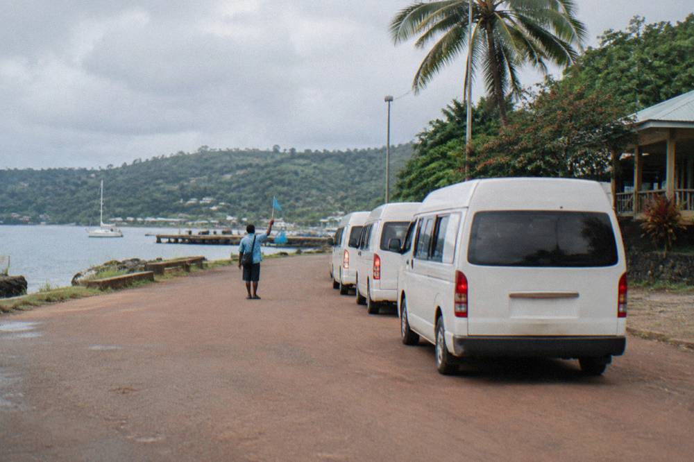 Orange tour flag held up beside a queue of minibuses at a Port Vila cruise wharf pickup point