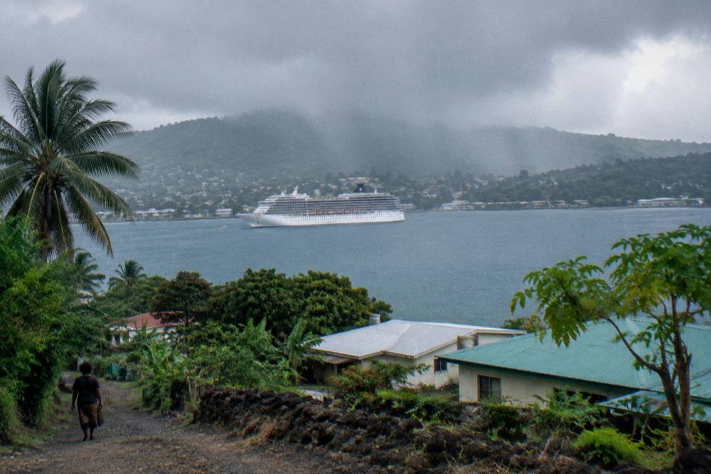 Cruise ship at anchor in a wide tropical bay with rain clouds passing over green hills